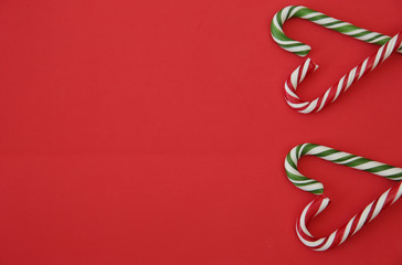 Christmas red background with caramel candy sugar canes folded in the form of a heart. Caramel sugar cane concept. Copy space for text. Flat lay. Pattern, card, frame. Valentine day. 