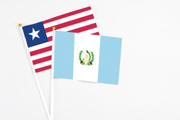 Fototapeta premium Guatemala and Liberia stick flags on white background. High quality fabric, miniature national flag. Peaceful global concept.White floor for copy space.