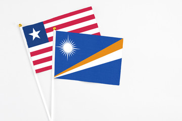 Fototapeta premium Marshall Islands and Liberia stick flags on white background. High quality fabric, miniature national flag. Peaceful global concept.White floor for copy space.