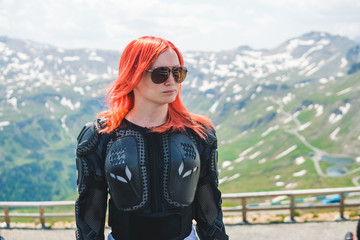 Close up portrait of a girl in full body protection, turtle armor jacket, on a background of green mountains with snowy top peaks, summer sunny day, rady to ride for adventure. safe outfit, equipment - obrazy, fototapety, plakaty