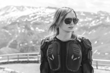 Close up portrait of a girl in full body protection, turtle armor jacket, on a background of green mountains with snowy top peaks, summer sunny day, rady to ride for adventure. black and white