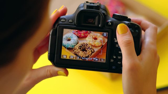 Close up - Food photographer take pictures with dslr camera of colored fresh donuts in box on yellow background. 4k. Concept of food photo blogging.