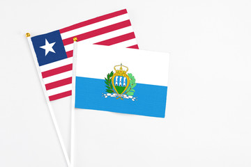 San Marino and Liberia stick flags on white background. High quality fabric, miniature national flag. Peaceful global concept.White floor for copy space.