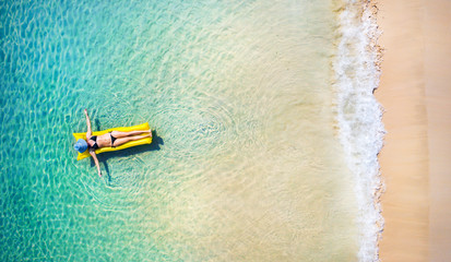 Young woman in hat relaxing on the yellow air mattress in tropical sea