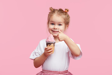 Cute child girl with pleasure eats tasty ice-cream on a pink studio background. Licks with closed...