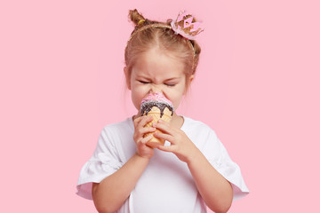 Cute child girl with pleasure eats tasty ice-cream on a pink studio background. Licks with closed eyes. The concept of baby food and a happy childhood