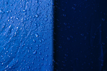 Water drops on waterproof nylon fabric. Macro detail view of texture of blue woven synthetic...