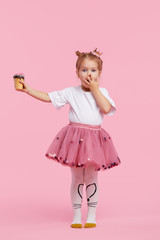 Cute child girl holds ice cream on his outstretched arm and covers his mouth with his hand. Refuses...