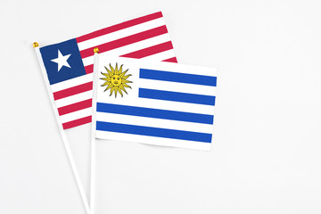 Uruguay and Liberia stick flags on white background. High quality fabric, miniature national flag. Peaceful global concept.White floor for copy space.
