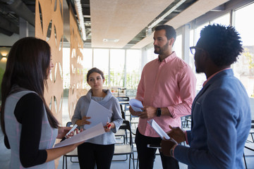 Multiethnic training group discussing their task. Young men and women in casual standing together, holding papers and markers, talking. Teamwork concept