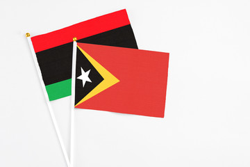 East Timor and Libya stick flags on white background. High quality fabric, miniature national flag. Peaceful global concept.White floor for copy space.