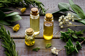 Aromatherapy. Essential oils in small bottles near fresh herbs on dark wooden background - obrazy, fototapety, plakaty