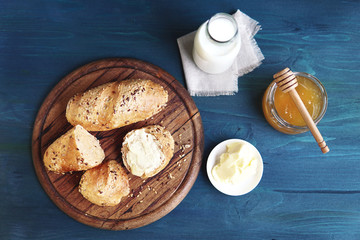   A fresh baked crunchy homemade bread with seeds, butter, bottle of milk, jar with honey. Healthy organic Breakfast on wooden table. Top view. Rustic still life.  