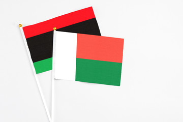 Madagascar and Libya stick flags on white background. High quality fabric, miniature national flag. Peaceful global concept.White floor for copy space.