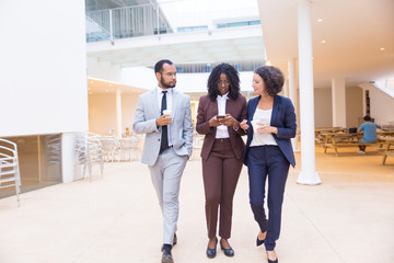 Serious business colleagues walking through office hallway. Business man and women using mobile phone, drinking coffee during work break. Corporate communication concept