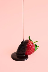 Minimal dark chocolate pouring drop to red strawberries on pastel pink background