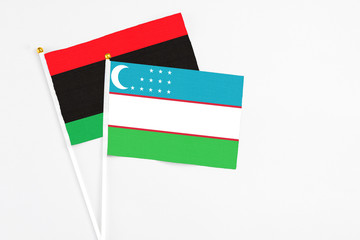Uzbekistan and Libya stick flags on white background. High quality fabric, miniature national flag. Peaceful global concept.White floor for copy space.