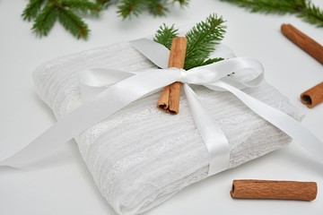Creative Christmas gift wrapping idea, present box wrapped in reusable white fabric, decorated with fir branch and cinnamon stick.
