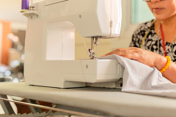 Old women hands stitching fabric on sewing machine at home.