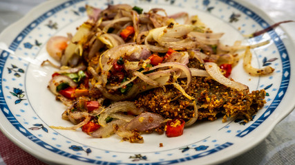 Fermented fried freshwater bream fish with fried onion or ikan pekasam in a plate on table.