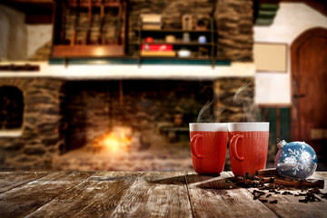 Christmas mugs with a hot drink. Steam smoke and Christmas decoration. Blurry background of a rustic fireplace with flame. American rifles on a stand. Place for your christmas gifts.Dark mood shadows.