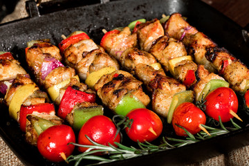 Grilled chicken skewers with spices and vegetables in a pan