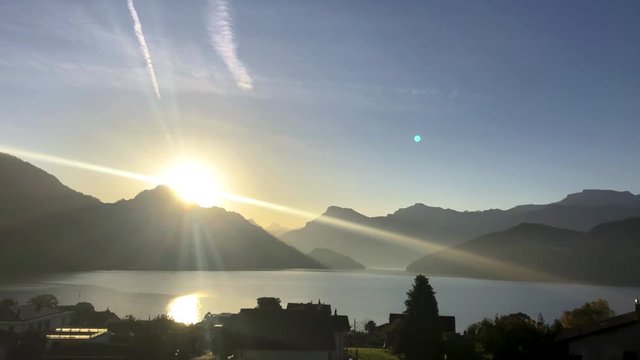 Sunrise over Lucerne lake in Switzerland with panoramic view of the Alps. First light rays seen from behind the mountain peak in Weggis town. Morning at a popular tourist destination.