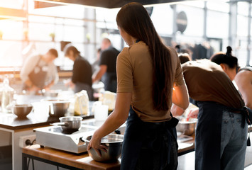 Culinary class. Back view of the process of cooking. Different unrecognizable people in gray apronsthe in the kitchen learn to cook