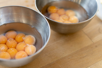 Two stainless steel bowls filled with many cracked eggs with whole yolks, in the wooden table. Close up