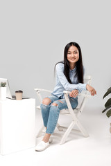 Freestyle. Asian girl isolated on white sitting at office posing to camera cheerful