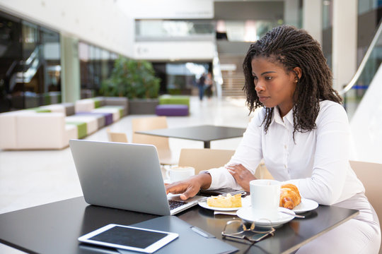 Serious Professional Watching Presentation On Laptop During Lunch. Young African American Business Woman Drinking Coffee In Cafe, Using Computer. Watching Content Concept