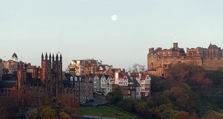 Fototapeta na wymiar Sunrise over Edinburgh Castle. The first sun rays hit the iconic buildings of the Old Town while a full moon is still showig in the early morning sky