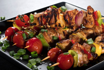 Grilled chicken skewers with spices and vegetables on plate and black background