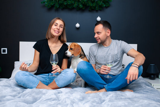 Young couple sitting on a bed in the bedroom, hugging. Near them is their dog