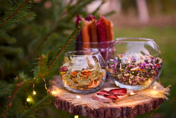 Collection of healing herbs in a glass bowl. Dry petals of tea rose and linden tree flowers. Alternative medicine, herbal treatments. Photo taken on a background of a summer forest.