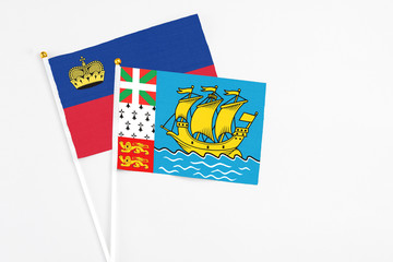 Saint Pierre And Miquelon and Liechtenstein stick flags on white background. High quality fabric, miniature national flag. Peaceful global concept.White floor for copy space.