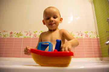 Happy little boy in the bathroom playing with plastic toy boat. Infant training and bathing. Hygiene and care for young children.