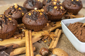 Chocolate holiday cupcakes, muffins with cake sprinkles on a wooden board, chocolate, cinnamon sticks, star anise, cocoa, nuts, burlap sack