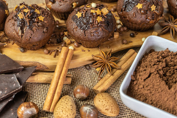 Obraz na płótnie Canvas Chocolate holiday cupcakes, muffins with cake sprinkles on a wooden board, chocolate, cinnamon sticks, star anise, cocoa, nuts, burlap sack