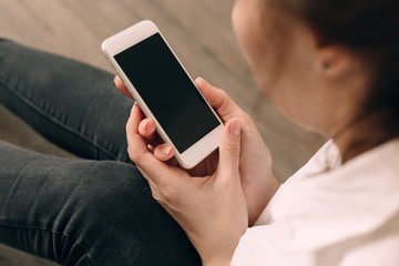 Woman hand holding white mobile phone and sitting on sofa at home.