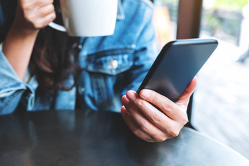 Closeup image of a woman holding  and using mobile phone while drinking coffee