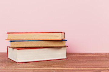 A simple composition of many hardback books, raw books on a wooden table and a pale pink background