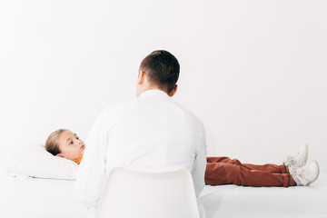 back view of pediatrist in white coat examining child in clinic