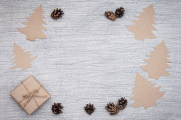 Christmas composition. Craft christmas trees, gift, pine cones on grey background. Frame, copy space, flat lay.