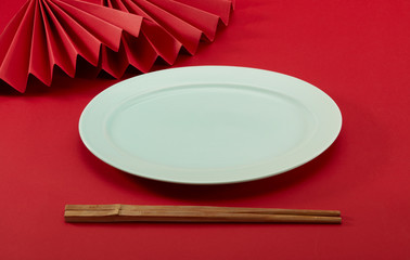 Chinese style chopsticks with red background and red folding fan and light green oval plate and...
