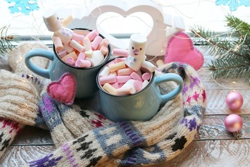A pair of cups with a drink decorated with meringues and marshmallow snowmen, Christmas decor, hearts, a knitted scarf on the windowsill, the concept of home comfort, winter holidays