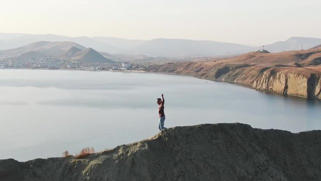 A man does morning sport exercises on a hill against the background of the sea.
