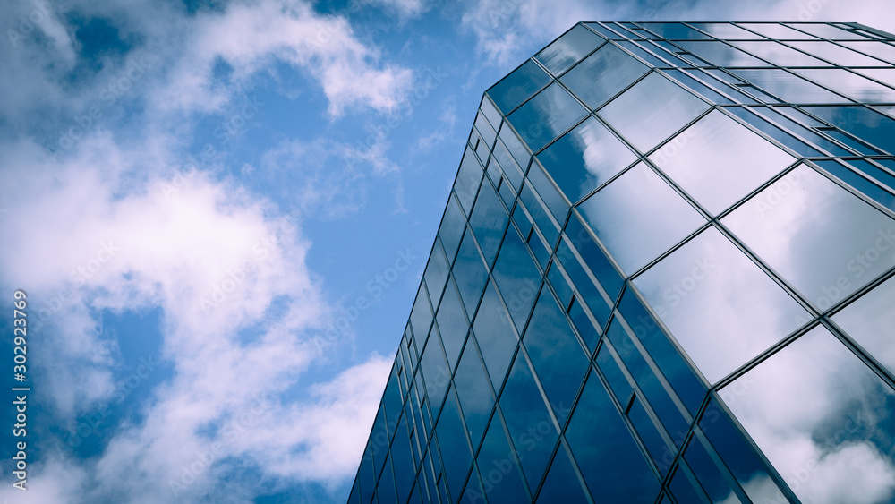 Wall mural Futuristic Business. Low angle view of a glass and steel skyscraper blending into and reflecting the blue sky and clouds.