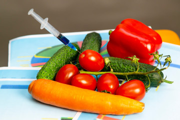 Syringes with chemicals on vegetables Two syringes with nitrates and pesticides lie on a box...