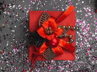 Present or red gift on festive background with confetti sparkles. Flat lay trendy style.